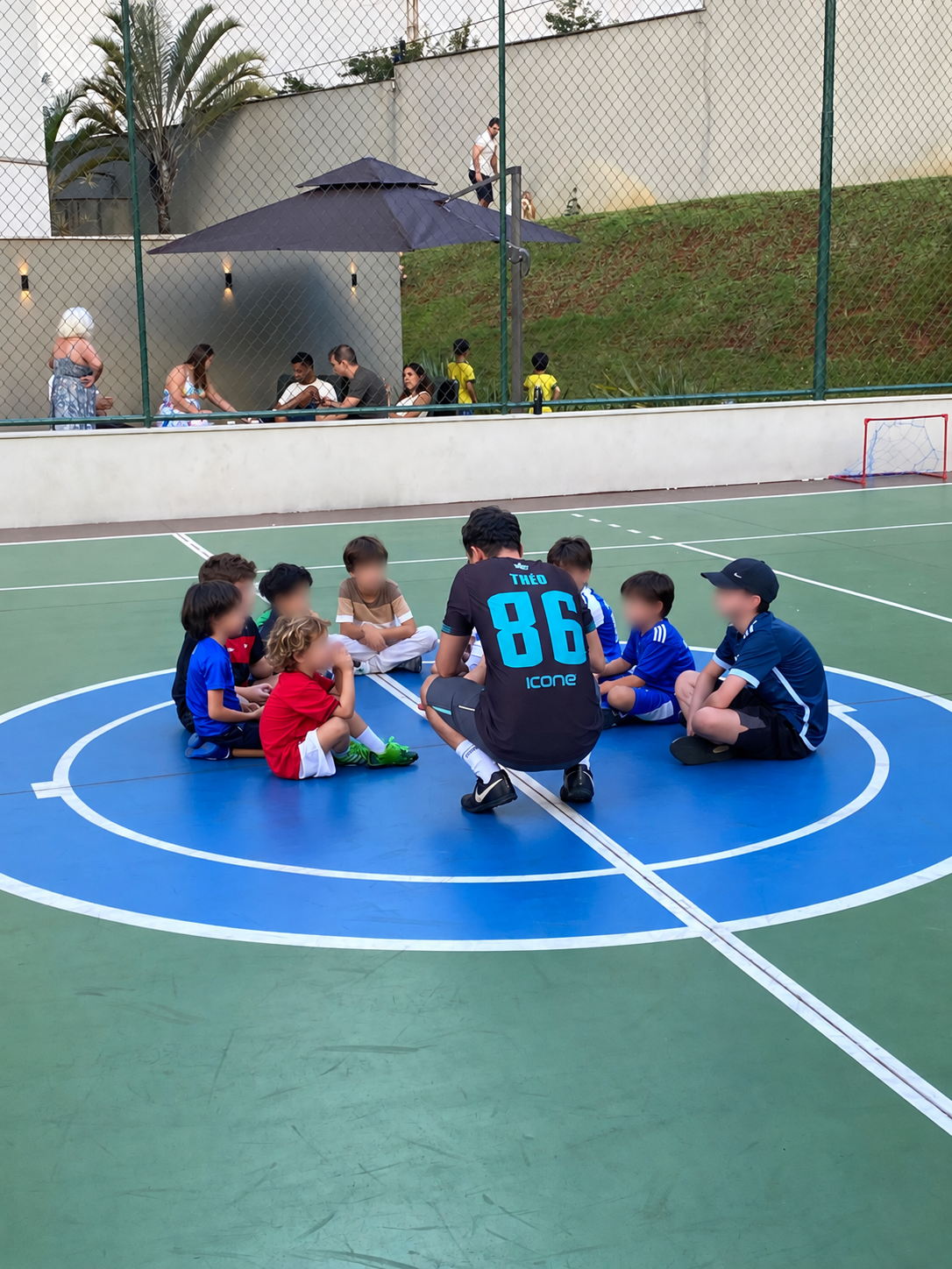 Turma de crianças em círculo na quadra com o coach da JT Esportes